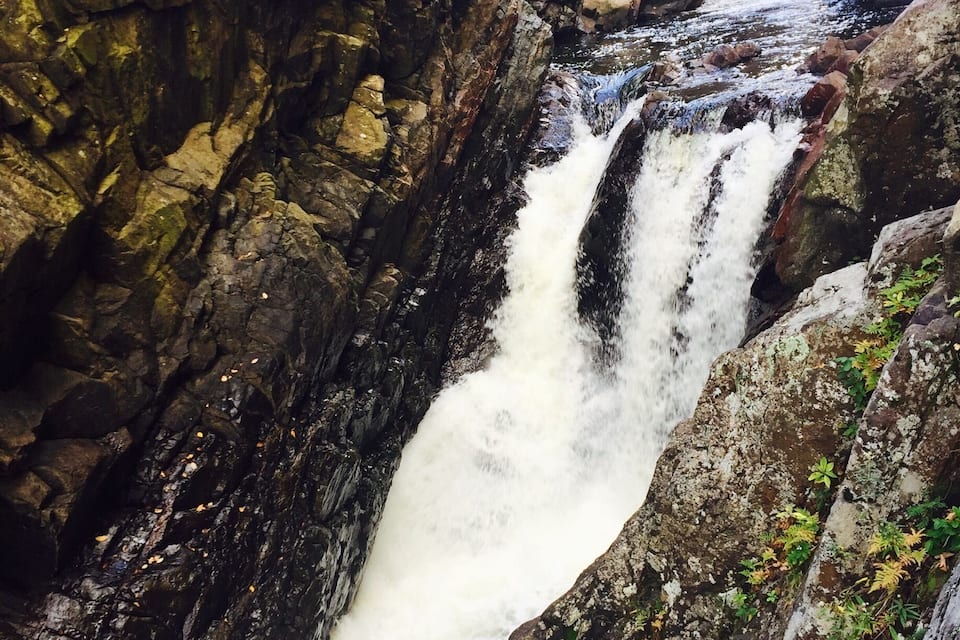 A waterfall cascading through a rocky gorge with moss-covered stones and a narrow stream.