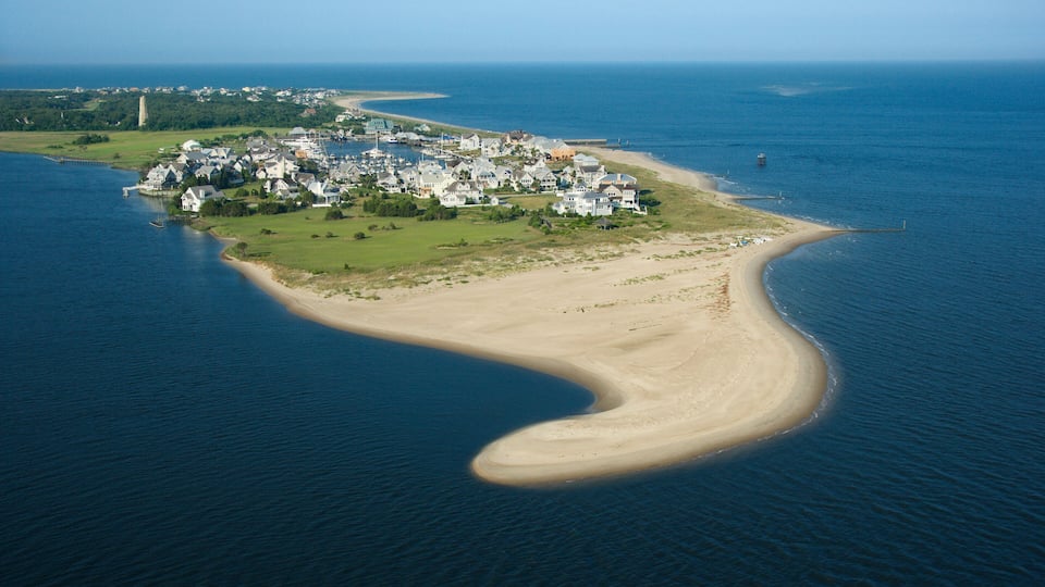 An aerial view of a coastal town with a curved shoreline, a lighthouse, and a large body of water.