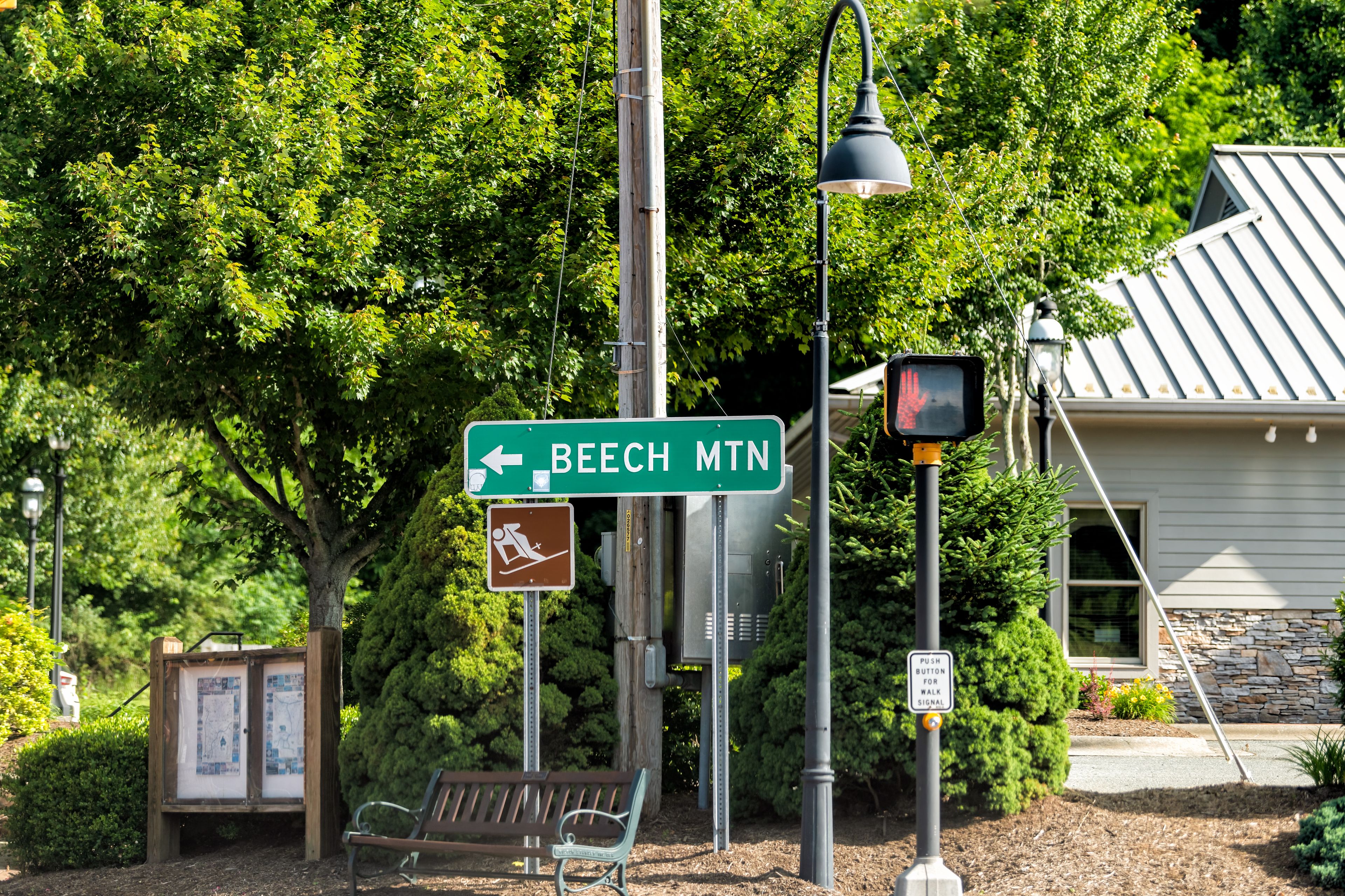 Una señal de calle indica BEECH MTN, un botón para el semáforo peatonal y un banco en un parque.