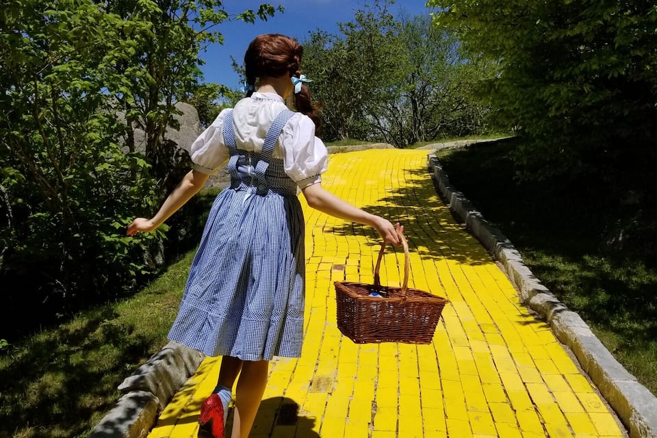 A person walking on a yellow brick road surrounded by greenery.