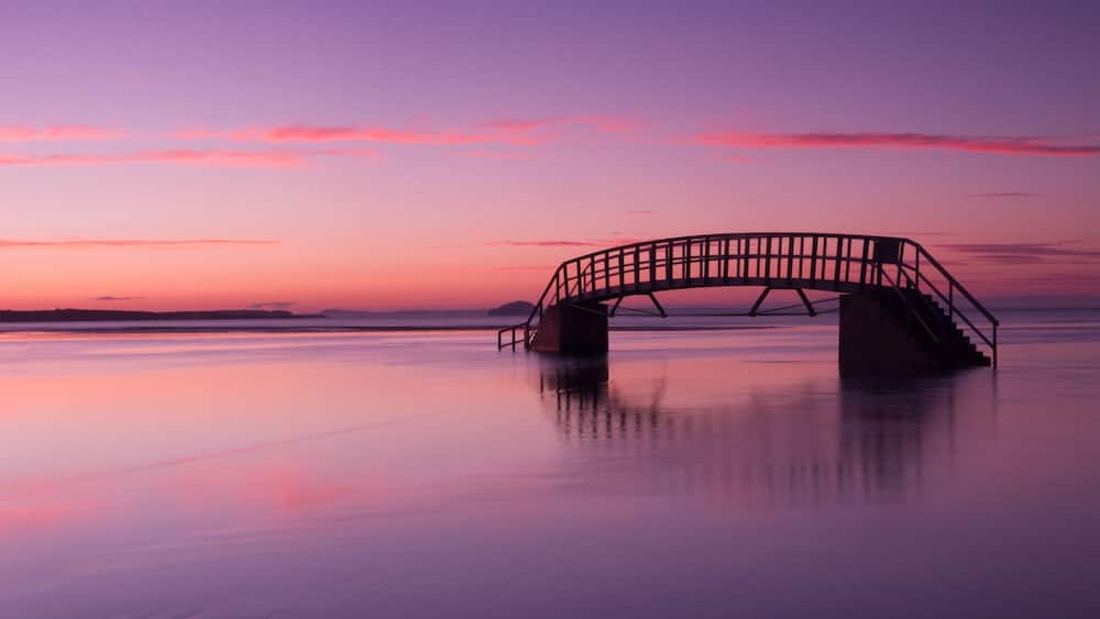A sunset over a calm lake with a bridge in the foreground.