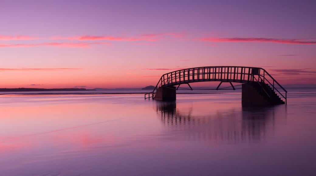 A sunset over a calm lake with a bridge in the foreground.