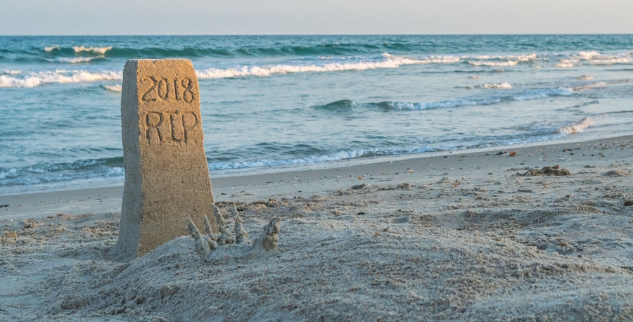 A sand marker with '2018 RIP' inscribed, a sandy beach, and waves in the background.