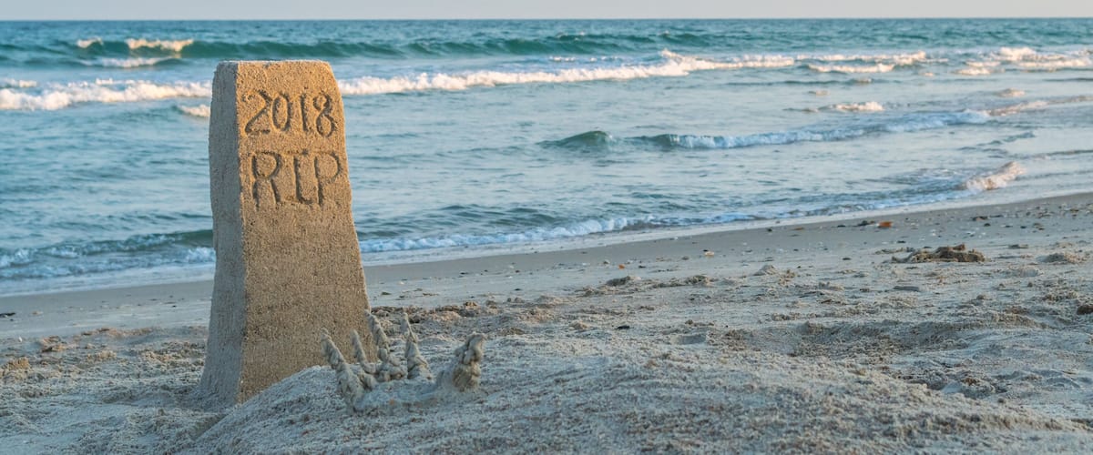 A sand marker with '2018 RIP' inscribed, a sandy beach, and waves in the background.