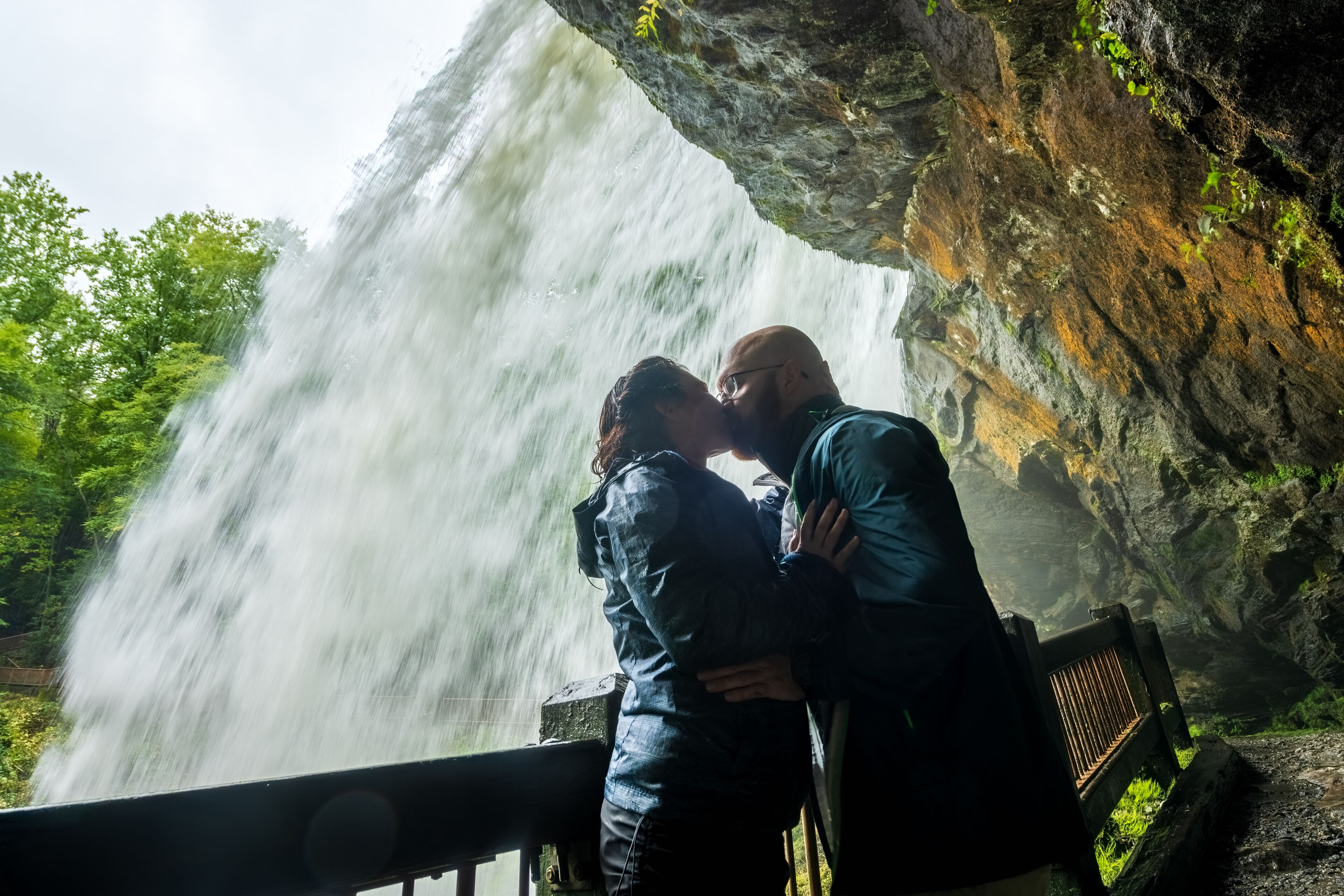 A waterfall, a couple embracing, and a rocky cliff.