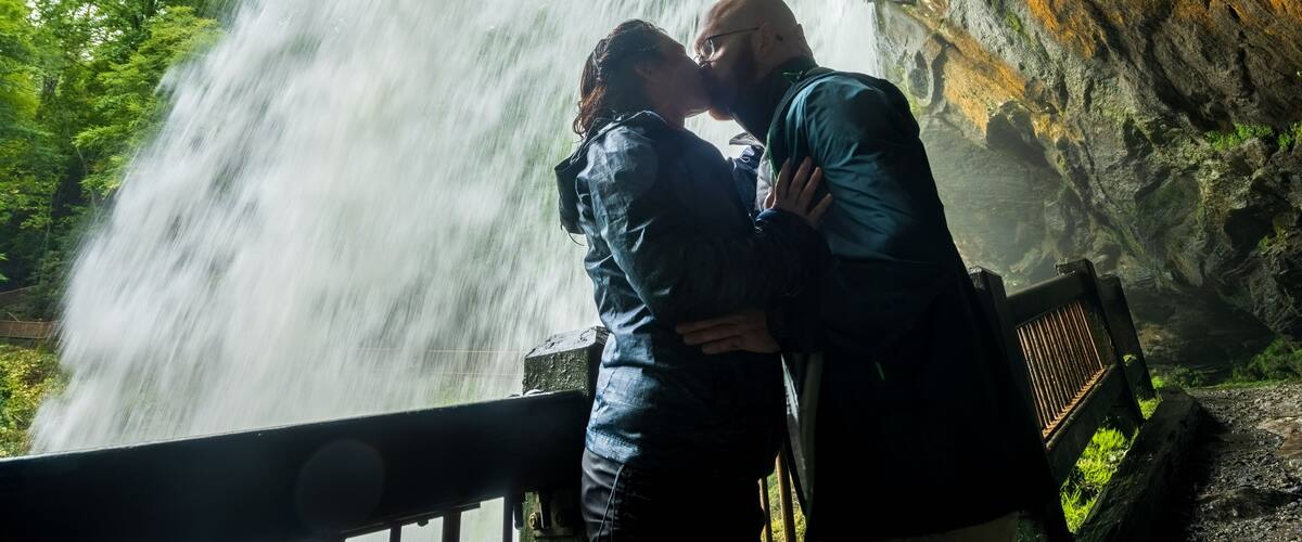 A waterfall, a couple embracing, and a rocky cliff.
