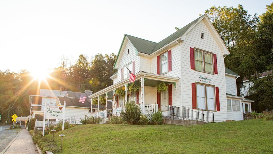 A white building with red shutters and a green roof, labeled "Nancy's Christmas Shop."
