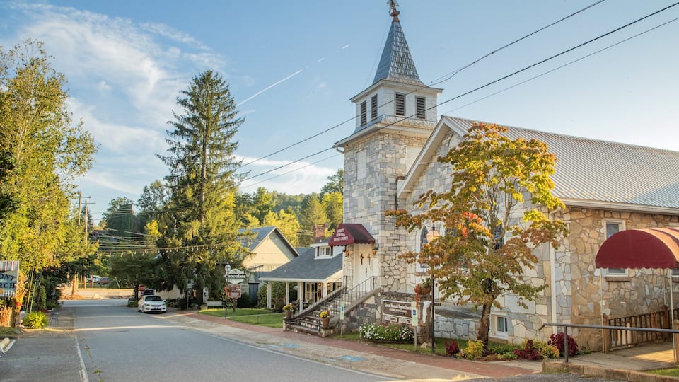 A stone church with a steeple, surrounded by trees and a road.