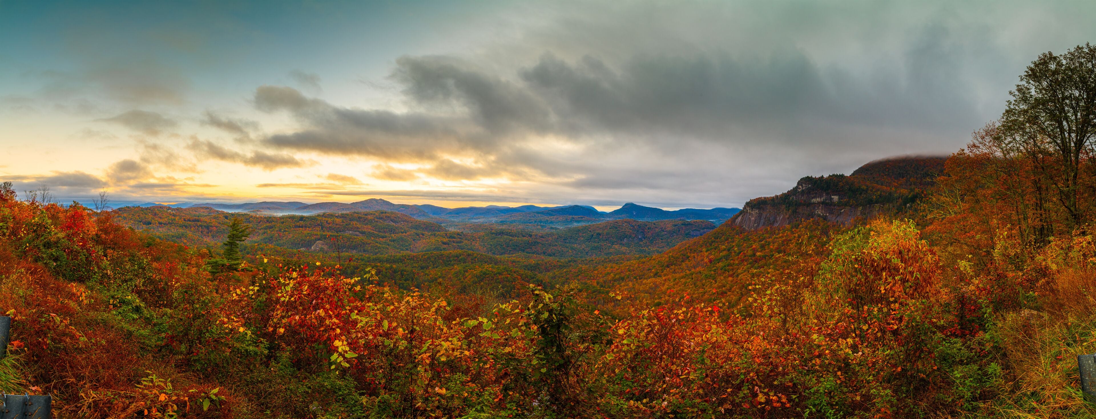 A mountainous landscape with autumn foliage, a cloudy sky, and distant mountains.