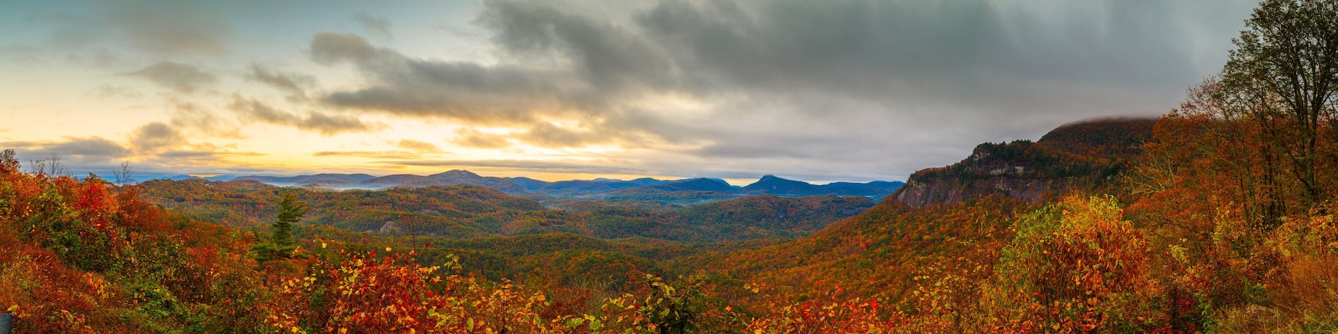 A mountainous landscape with autumn foliage, a cloudy sky, and distant mountains.