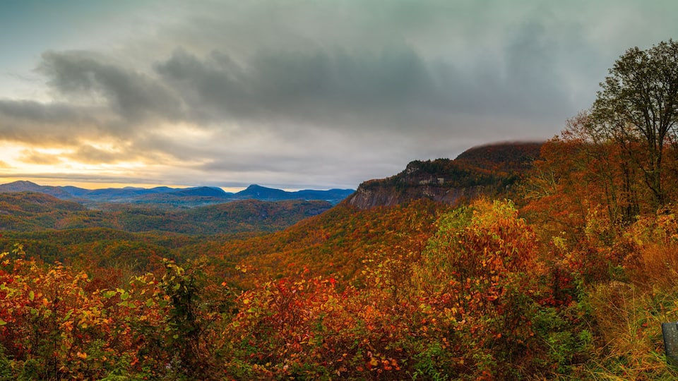 A mountainous landscape with autumn foliage, a cloudy sky, and distant mountains.