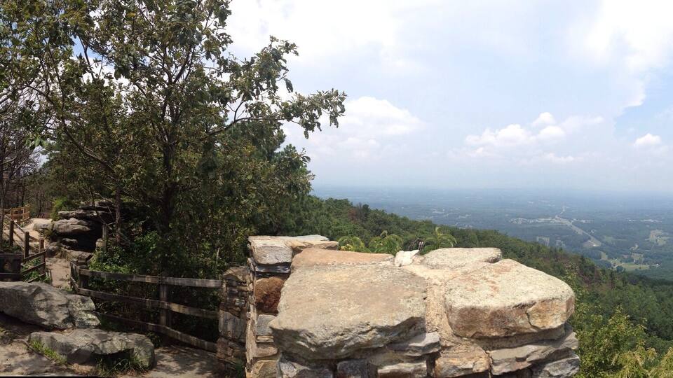 A mountainous landscape with a prominent rock formation in the center, surrounded by dense forest.