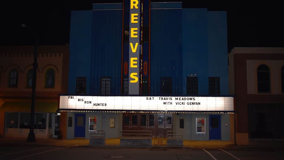 A theater with a marquee reading "REEVES" and a sign for "TRAVIS MEADOWS WITH VICKI GEFAN".