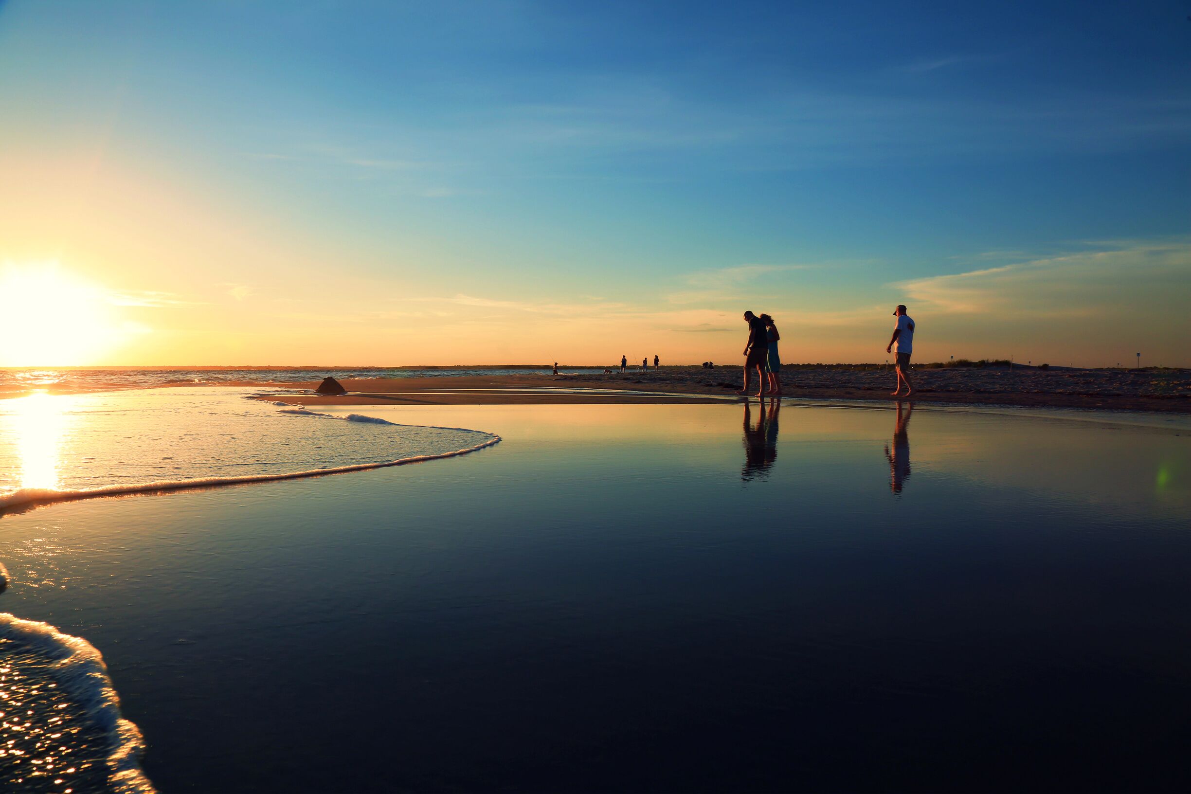 A beach at sunset with calm waters and a clear sky.