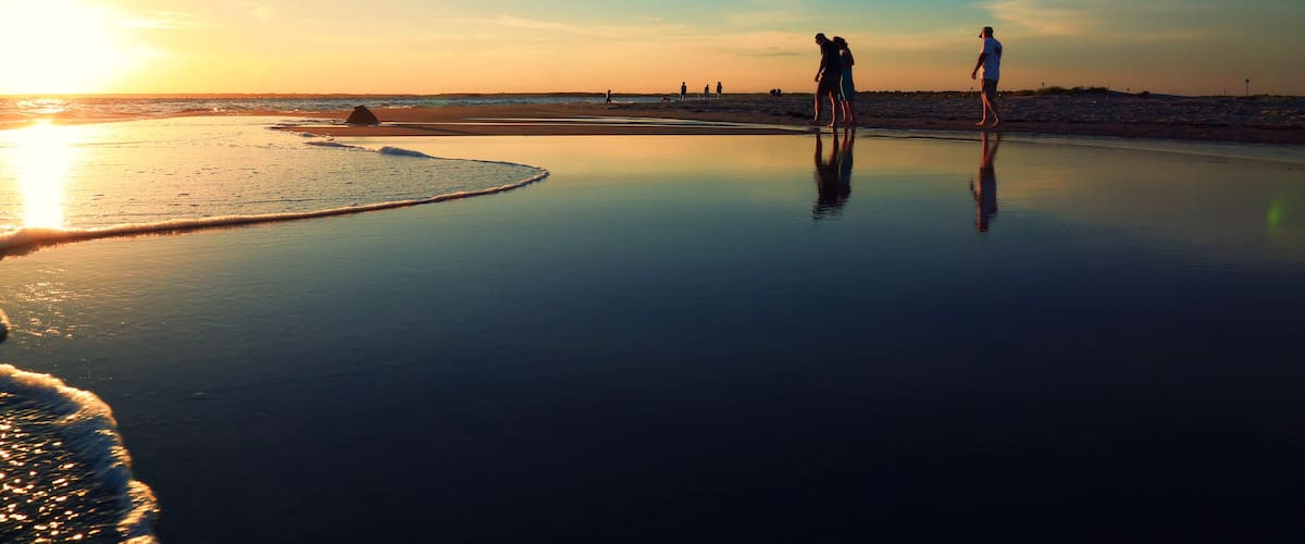 A beach at sunset with calm waters and a clear sky.