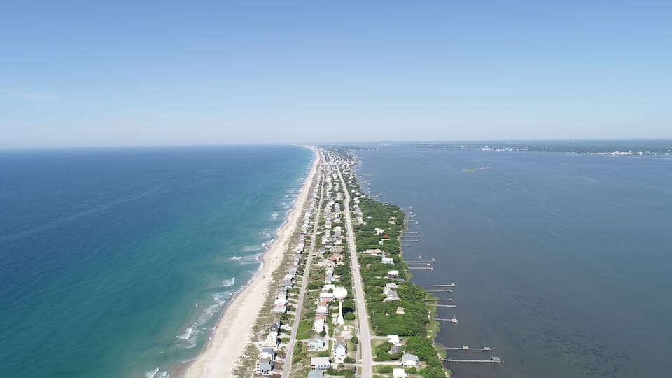 A coastal city with a long beachfront, dense residential area, and a clear sky.