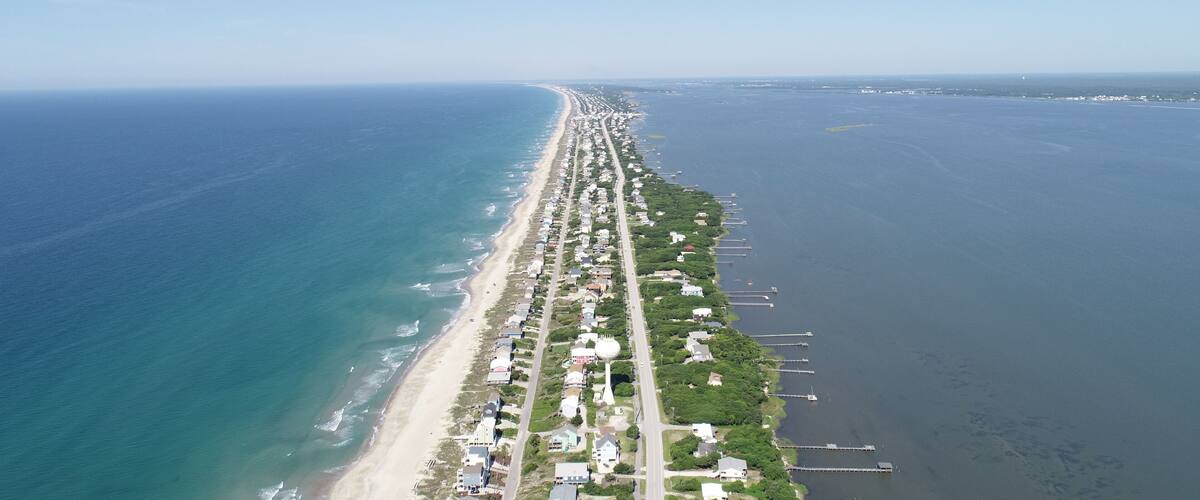 A coastal city with a long beachfront, dense residential area, and a clear sky.