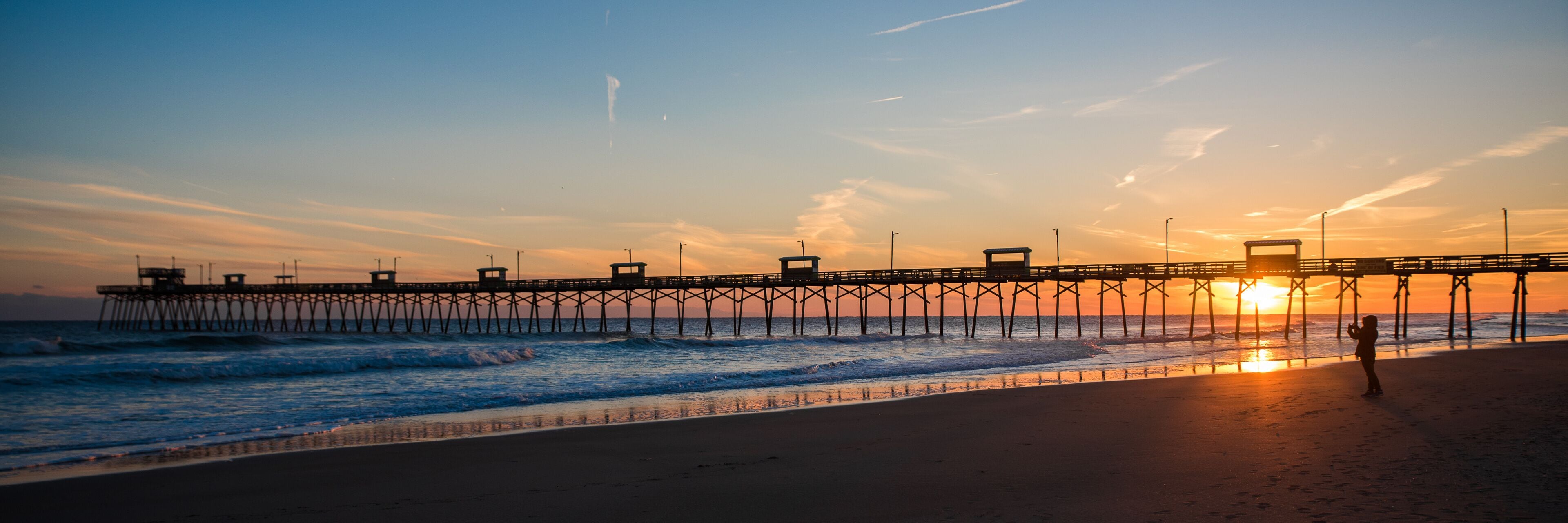 Colorful Sunset at ocean coast with silhouette of pier and photographer