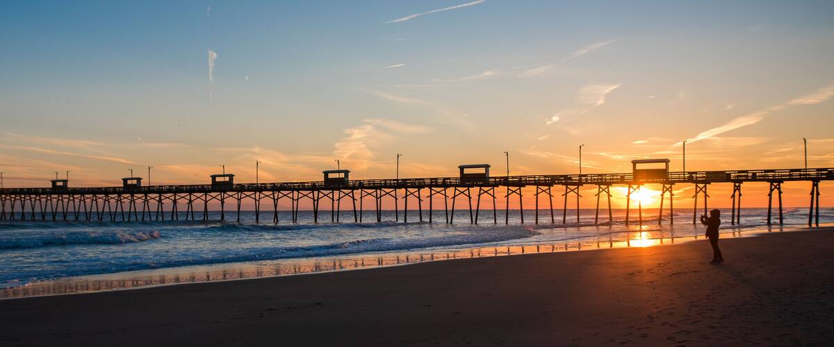 Colorful Sunset at ocean coast with silhouette of pier and photographer