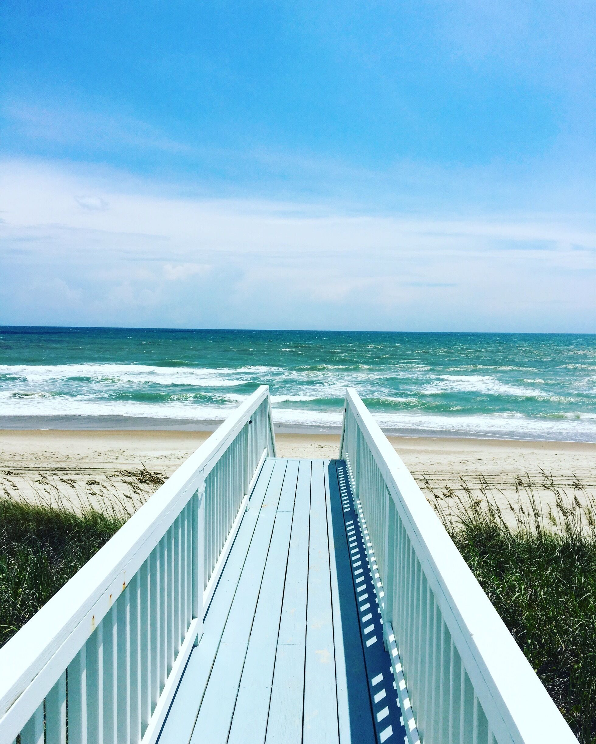 A wooden boardwalk leading to a beach with waves crashing onto the shore under a clear sky.