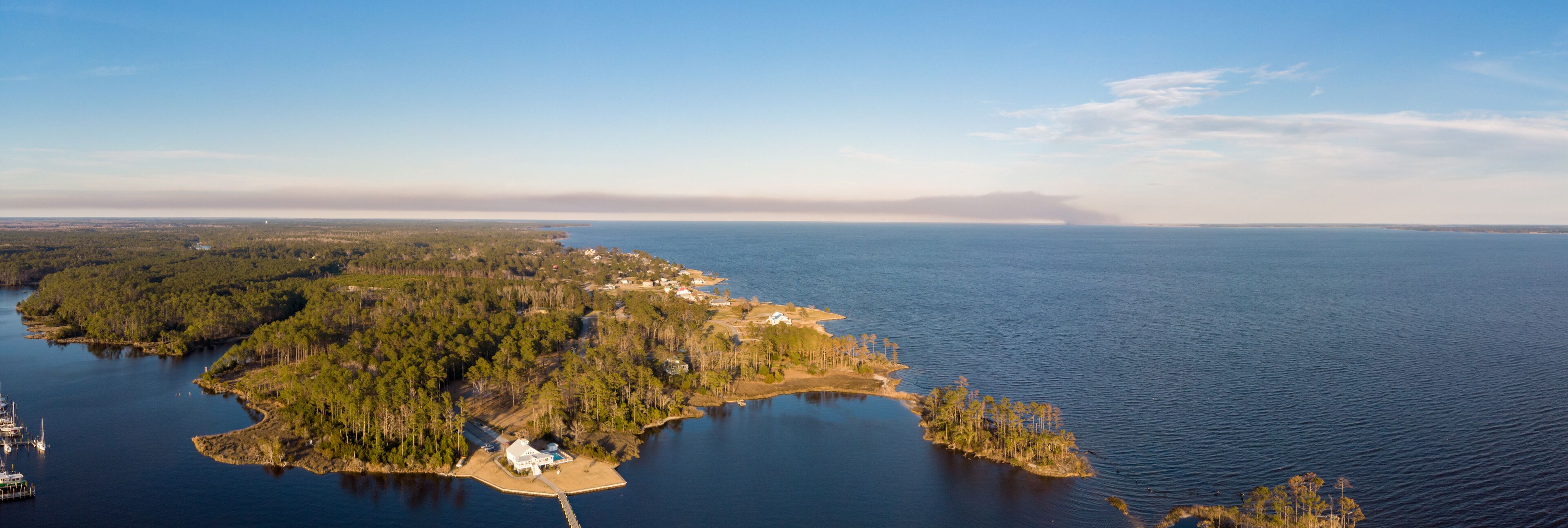 An aerial view of a coastal area with a small island surrounded by water, featuring dense forests, a marina, and a few buildings.