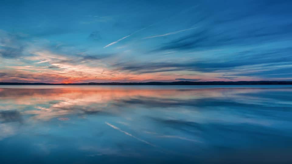 A calm lake reflecting a sunset sky with clouds.