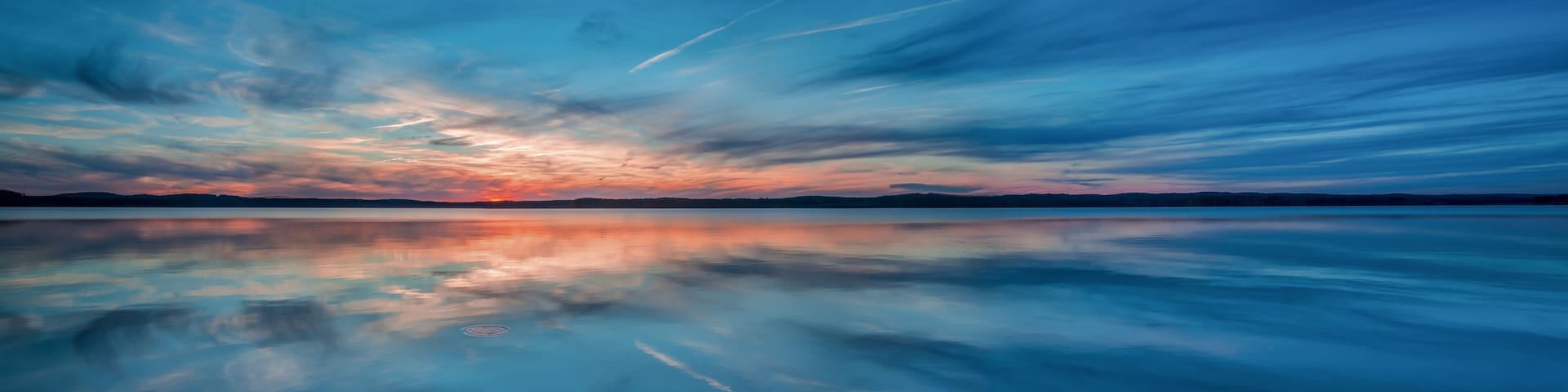 Ein stiller See spiegelt einen Sonnenuntergangshimmel mit Wolken.