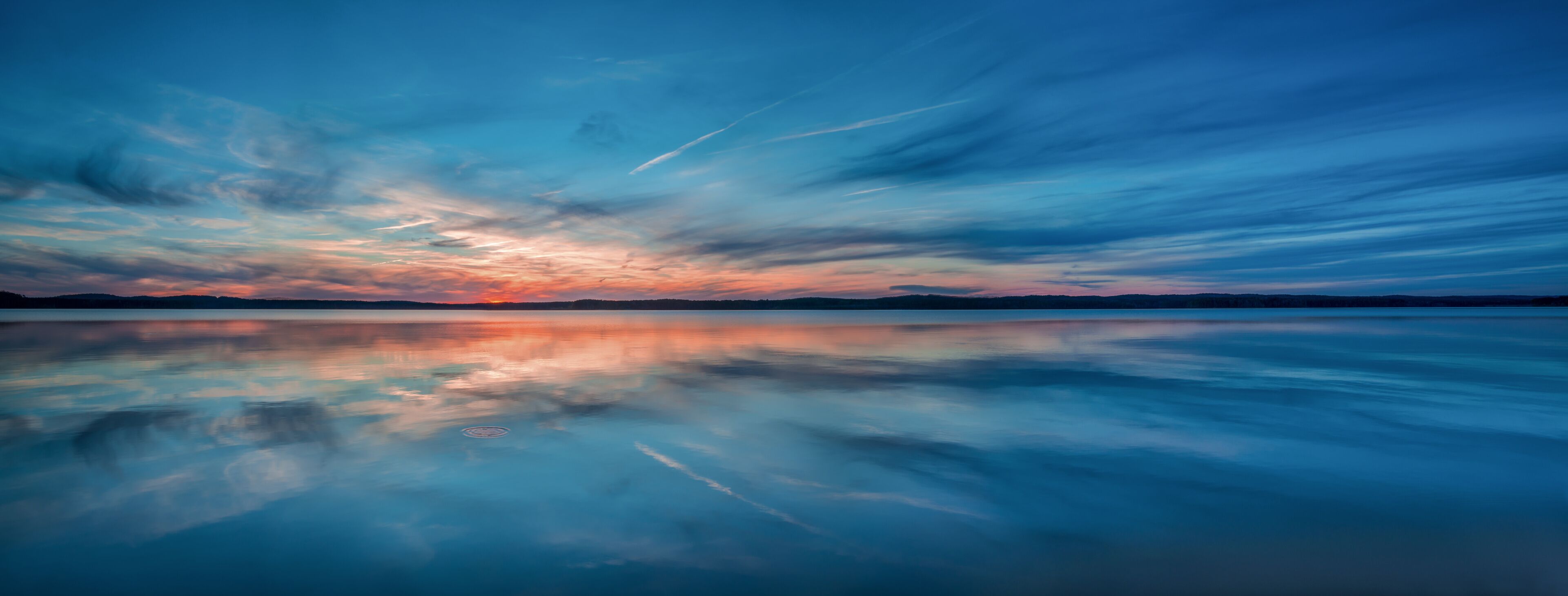 A calm lake reflecting a sunset sky with clouds.