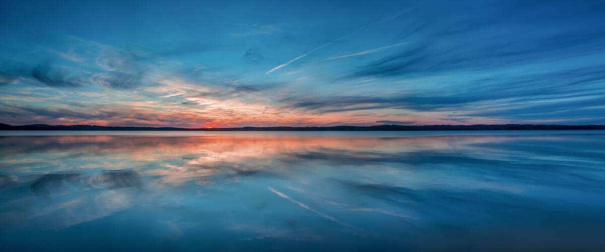 A calm lake reflecting a sunset sky with clouds.