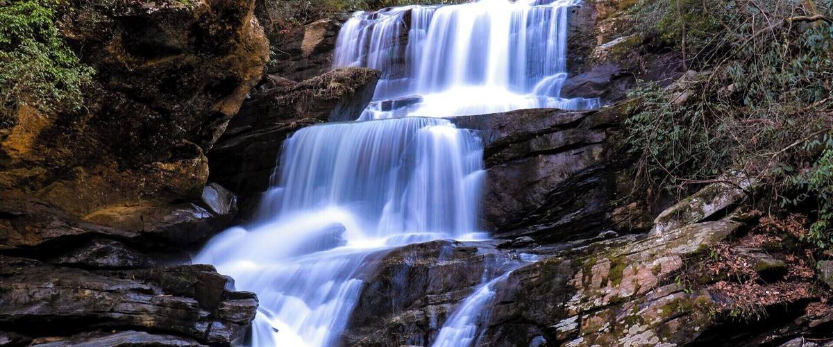 A multi-tiered waterfall cascading over rocky terrain with a calm pool at the base.