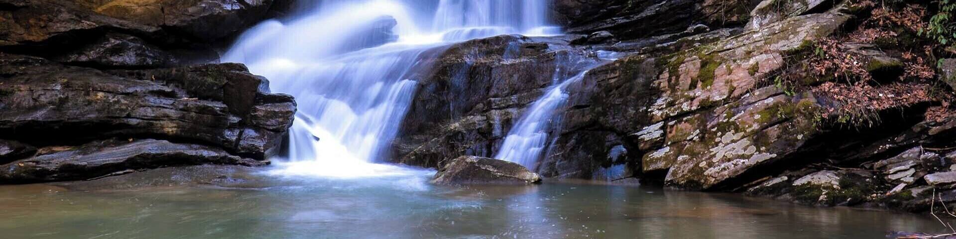 A multi-tiered waterfall cascading over rocky terrain with a calm pool at the base.