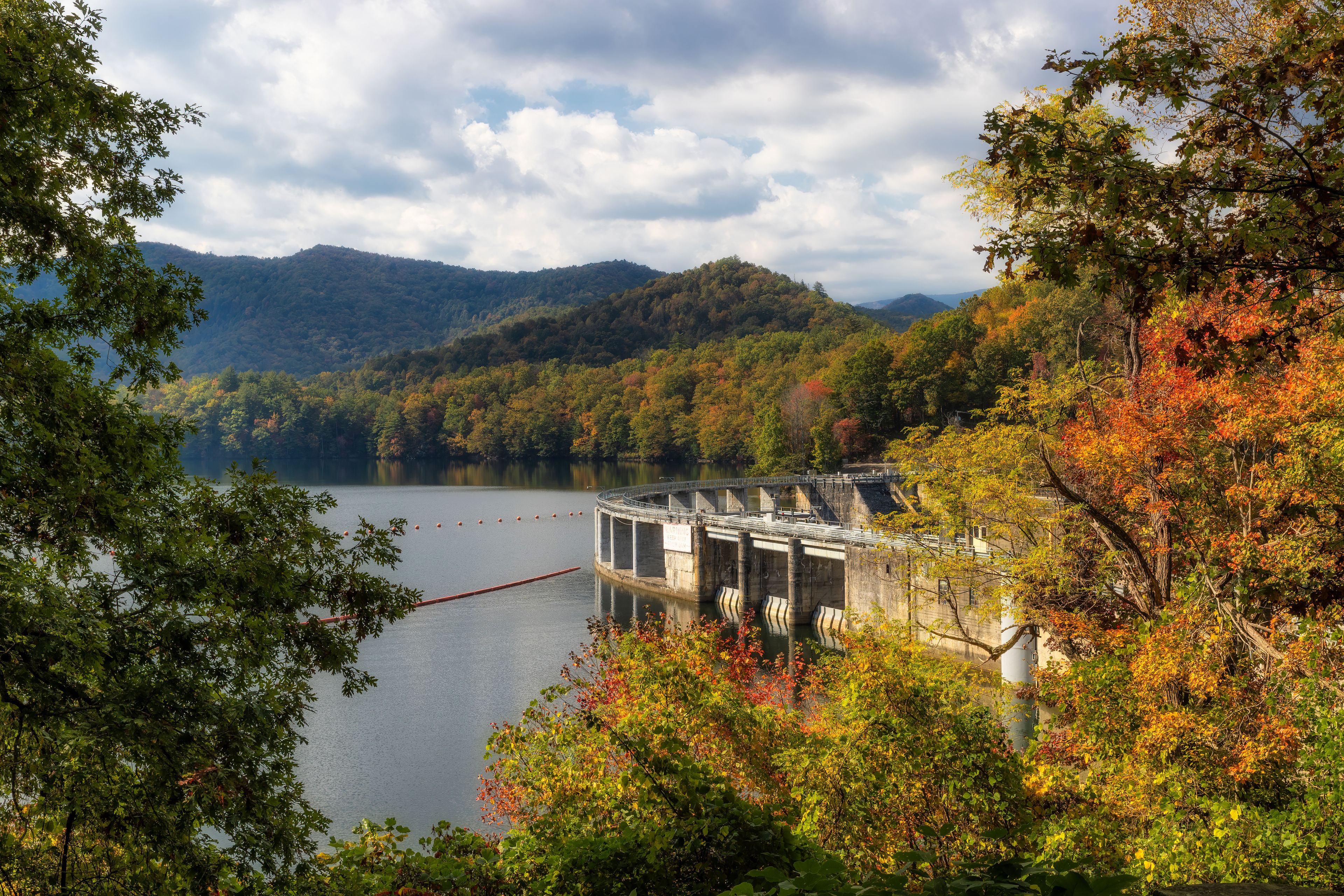 Ein Stausee mit einer Brücke, umgeben von Herbstlaub und Hügeln.