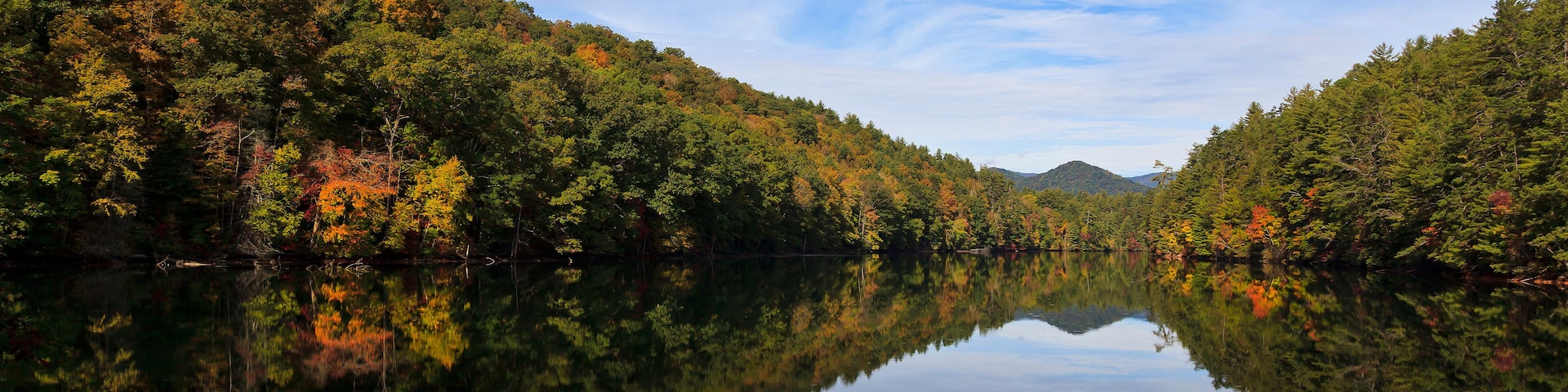 A calm lake reflecting the surrounding autumn foliage and a clear blue sky.