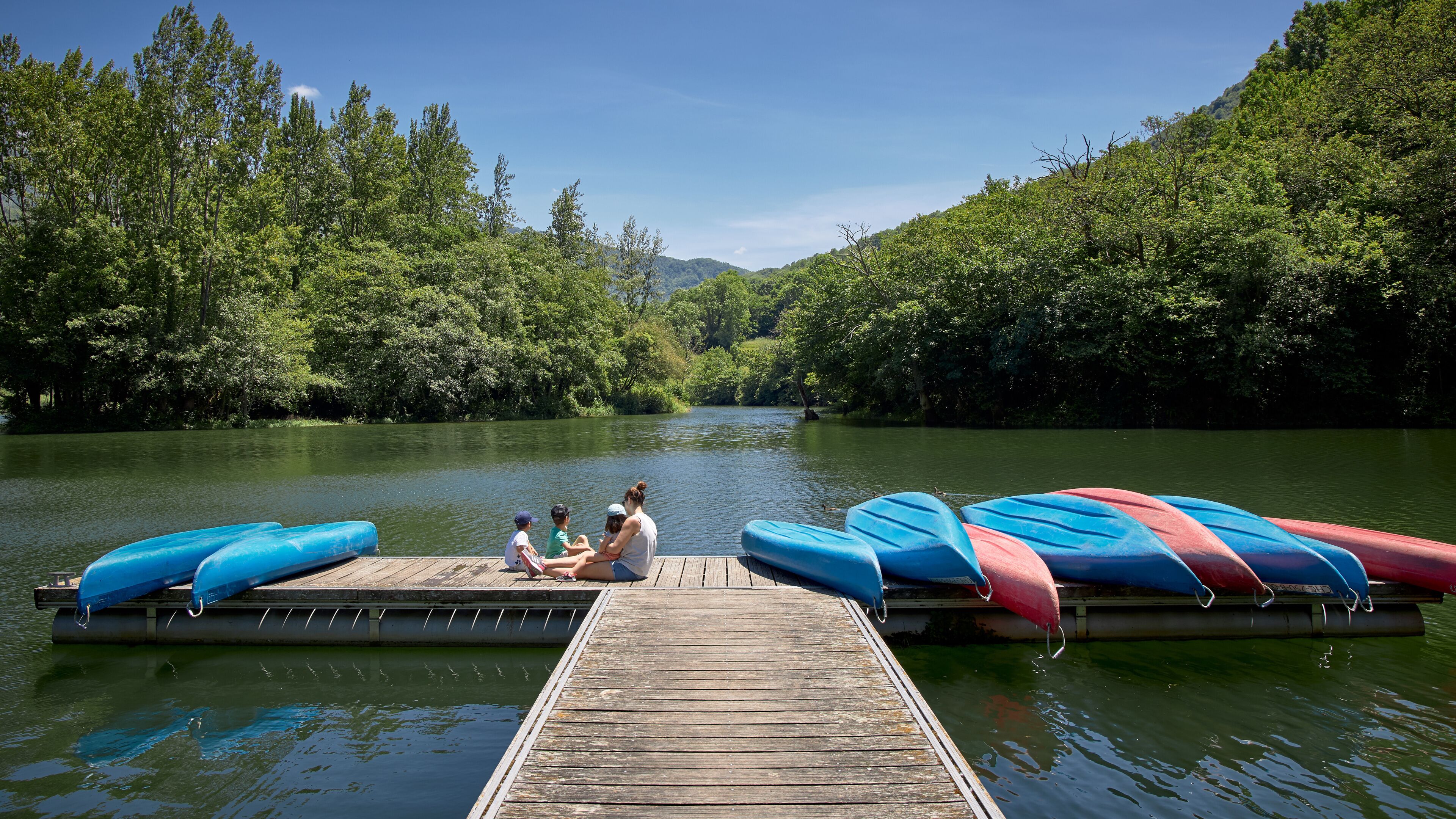 familia sentada en un embarcadero de un lago entre montañas