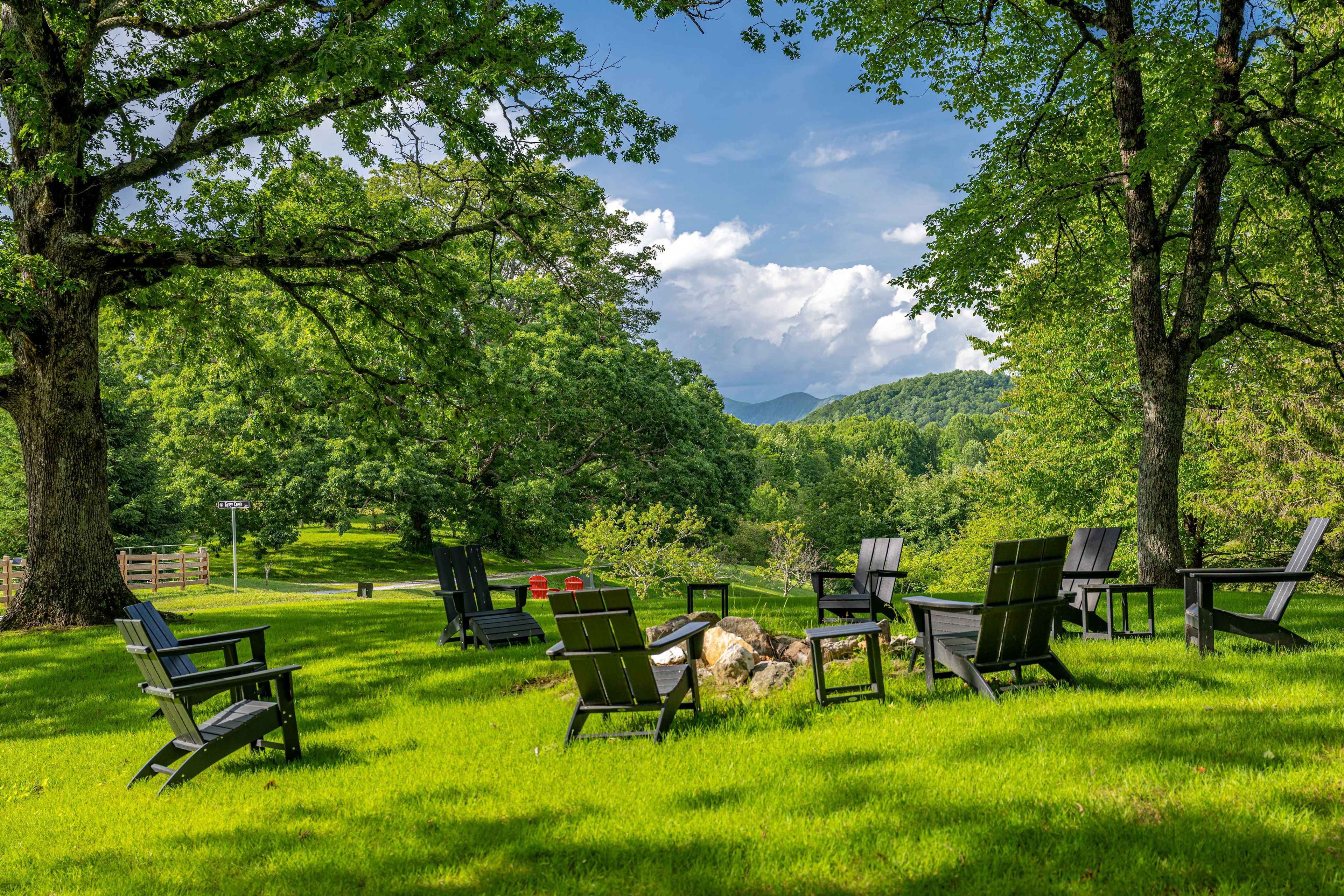 A park with green grass, trees, and Adirondack chairs.