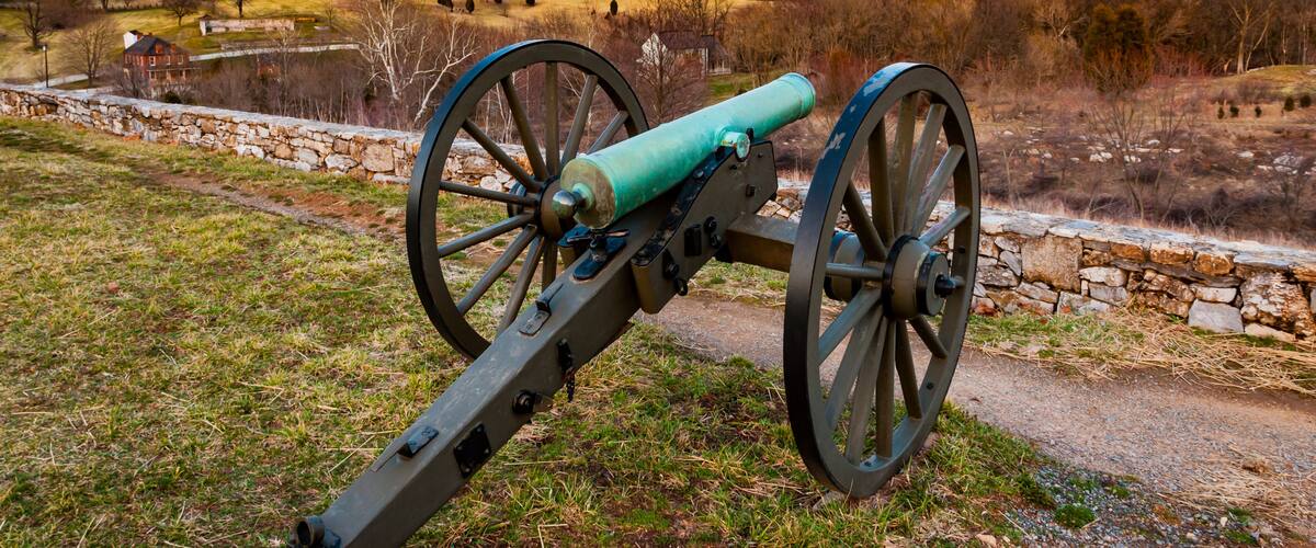 A cannon on a grassy field with a stone wall and a house in the background.