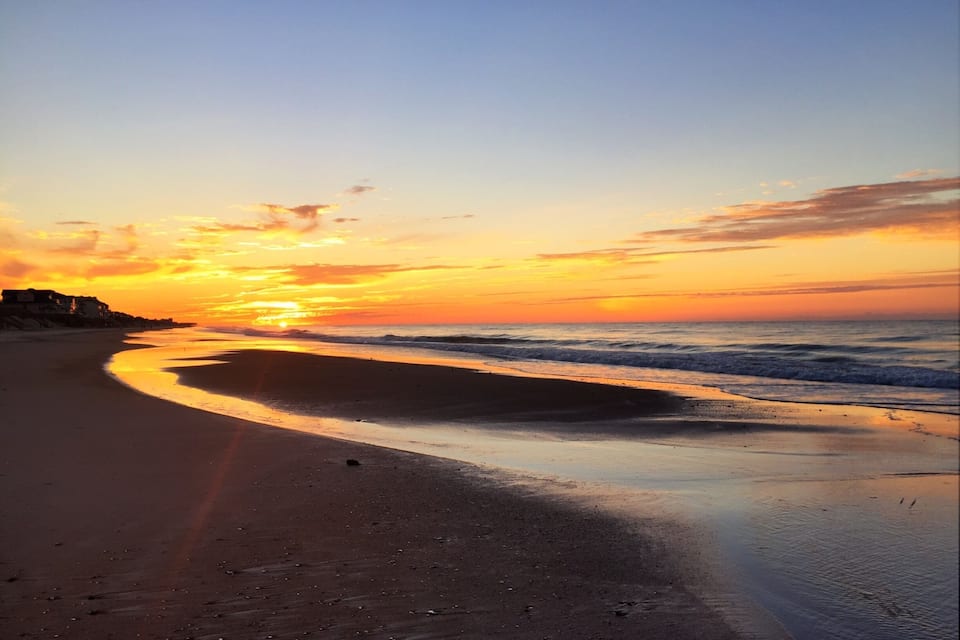 A beach at sunset with a curved shoreline and ocean waves.