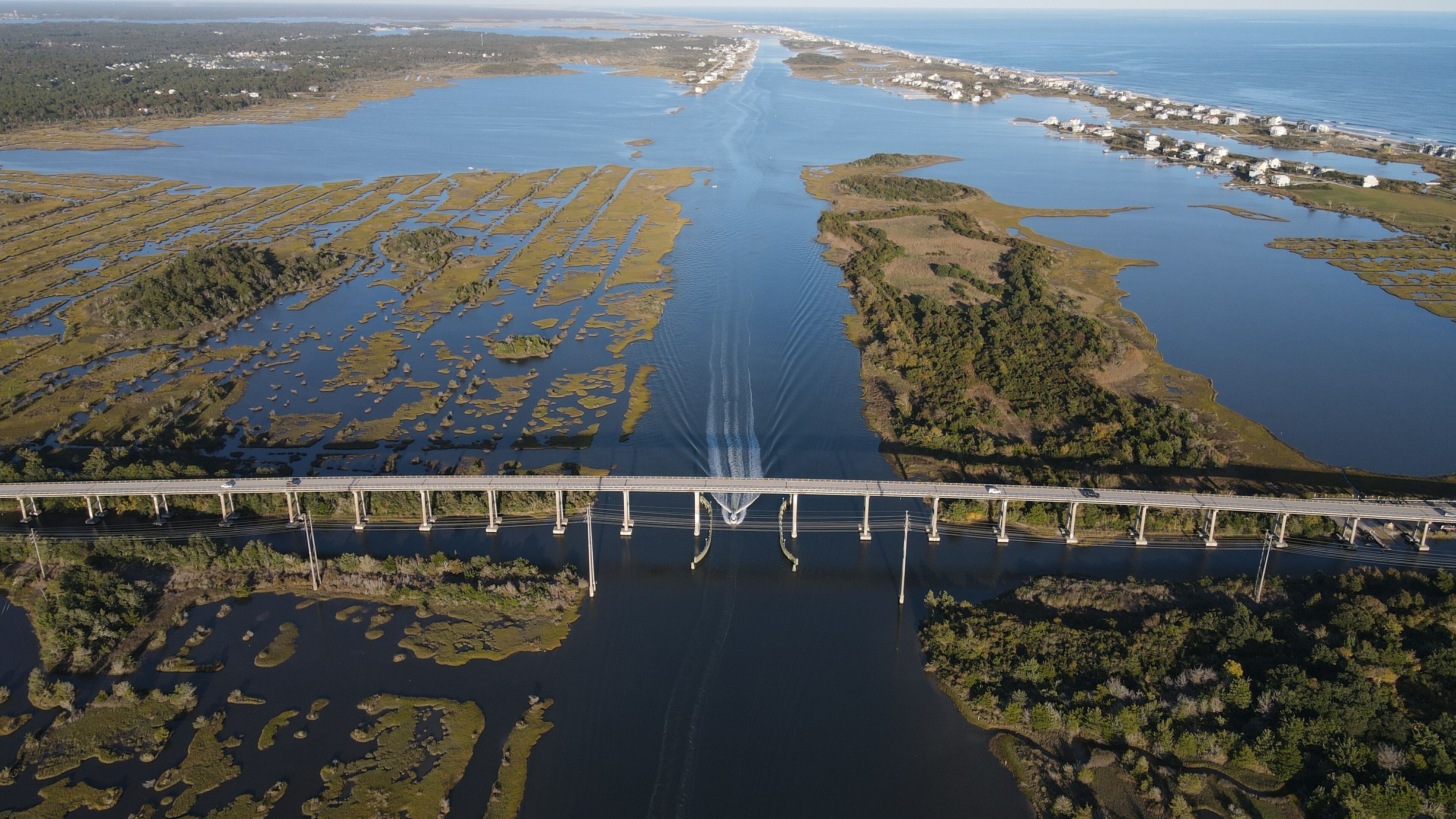 An aerial view of a bridge over a large water body with surrounding land and vegetation.