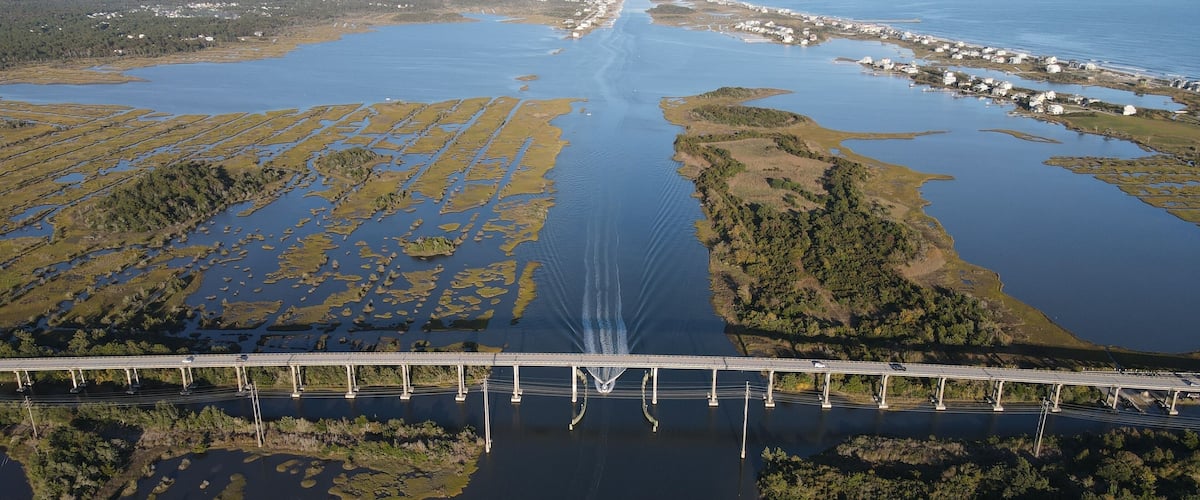 An aerial view of a bridge over a large water body with surrounding land and vegetation.