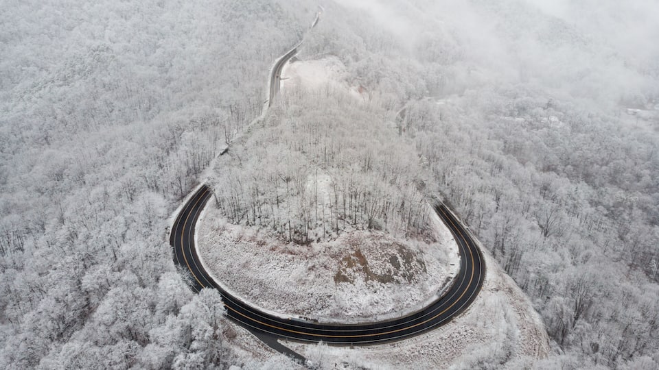 A snow-covered winding road through a forested mountain area.