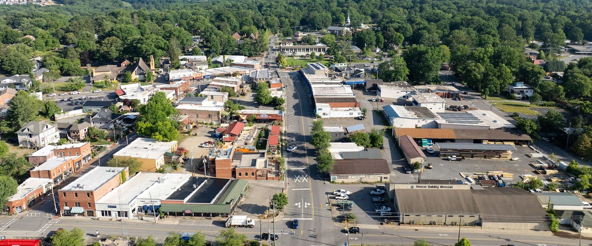 A town with a mix of commercial and residential buildings, surrounded by lush green mountains.