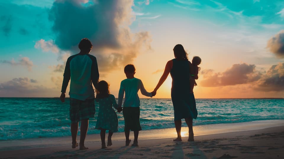 A family walking on a beach during sunset.