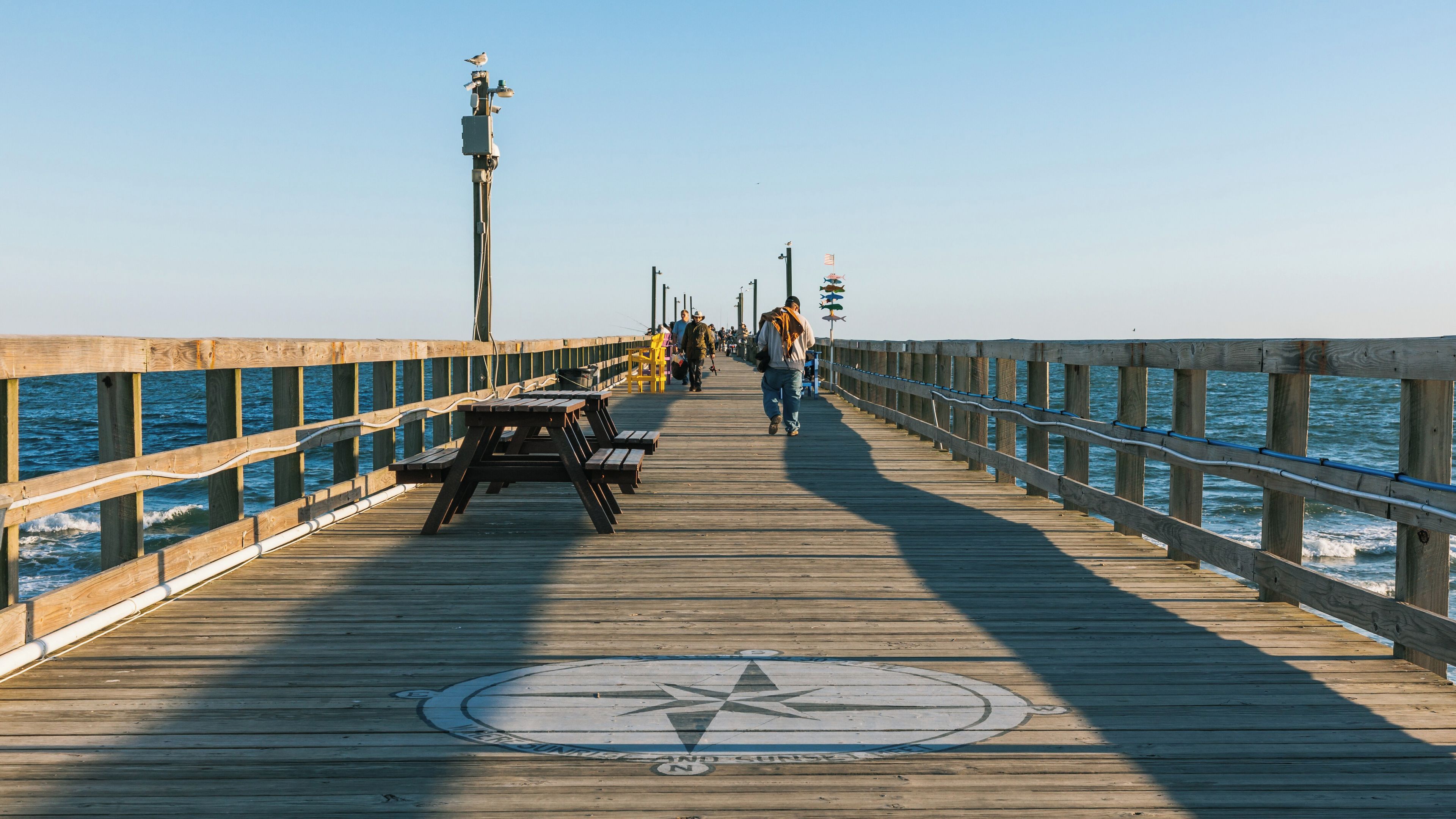 A wooden pier with a compass rose, benches, and people walking.