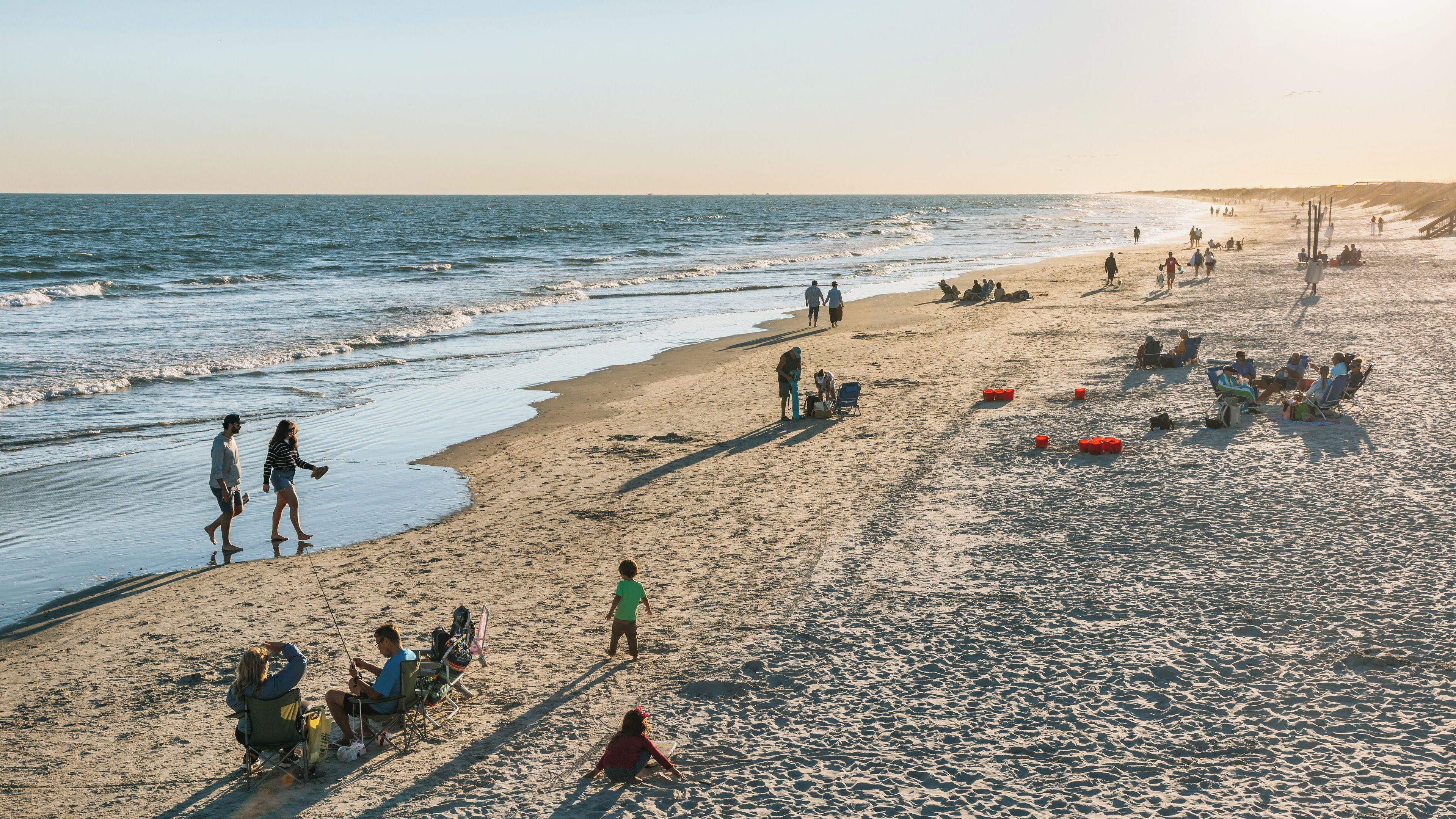 A beach with people walking, sitting, and fishing.