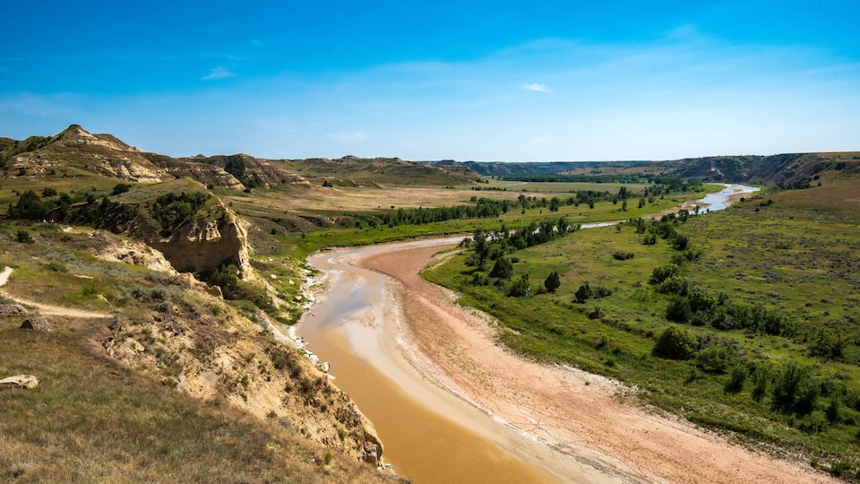 A river winding through a valley with green fields and a rocky hill on the left.