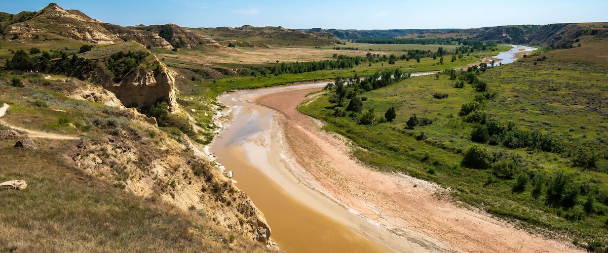A river winding through a valley with green fields and a rocky hill on the left.