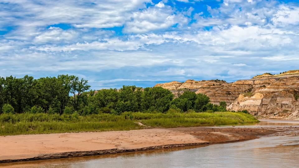 A river flowing through a canyon with layered rock formations and dense green vegetation on the banks.