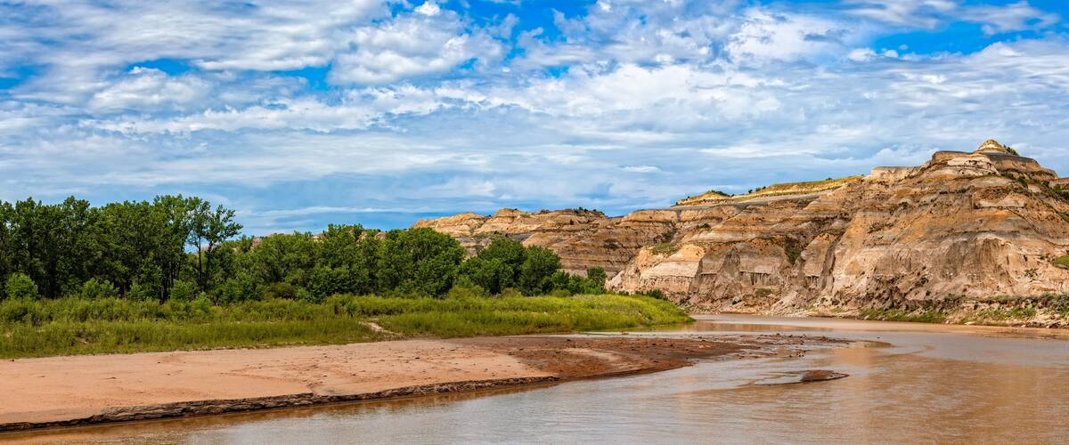 A river flowing through a canyon with layered rock formations and dense green vegetation on the banks.