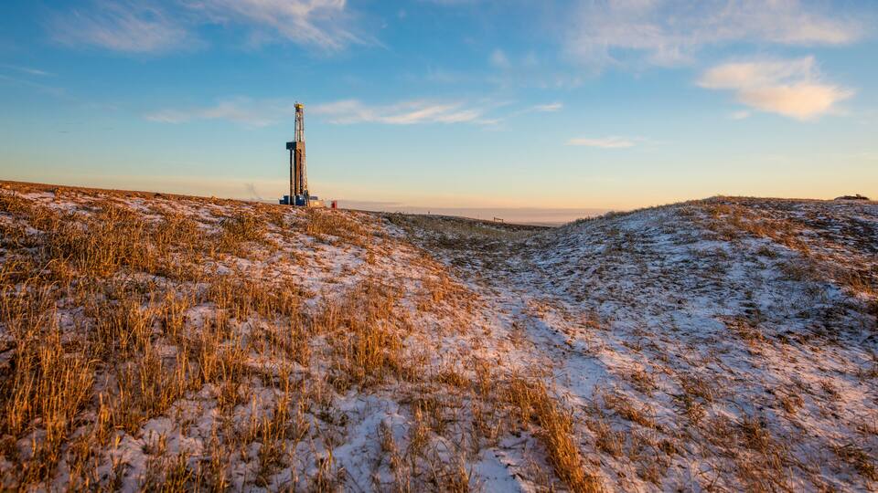 A snowy landscape with a drilling rig in the distance.