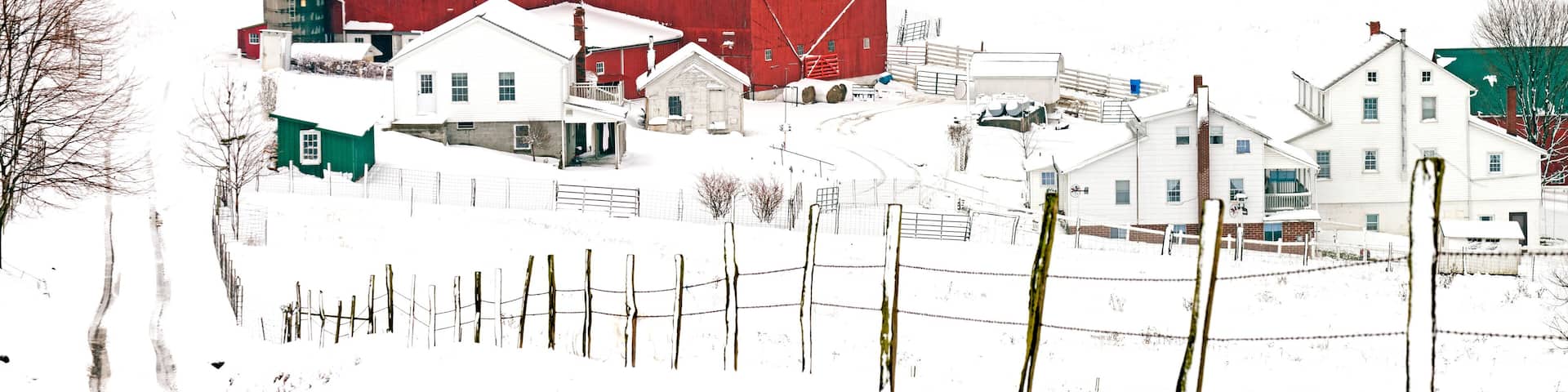 A snow-covered farm with a red barn, a silo, and several white houses.